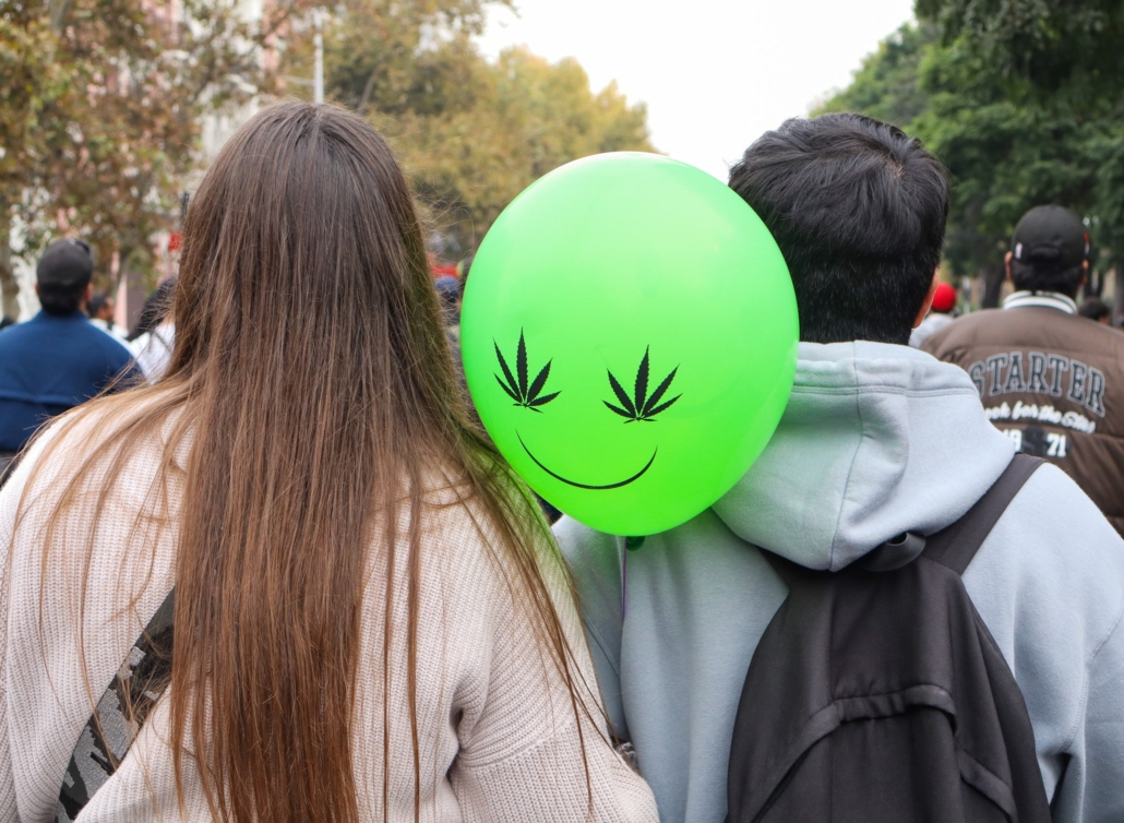 Una pareja de espalda y un globo con ojos de cannabis 