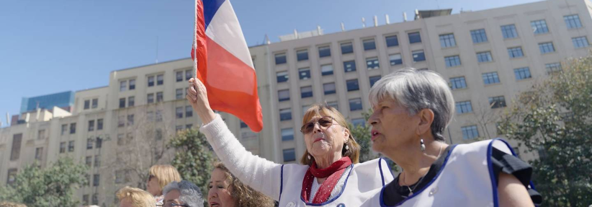 Deuda histórica profesores. Manifestaciones de profesores afectados frente al Palacio la Moneda, mujer levanta una bandera chilena.